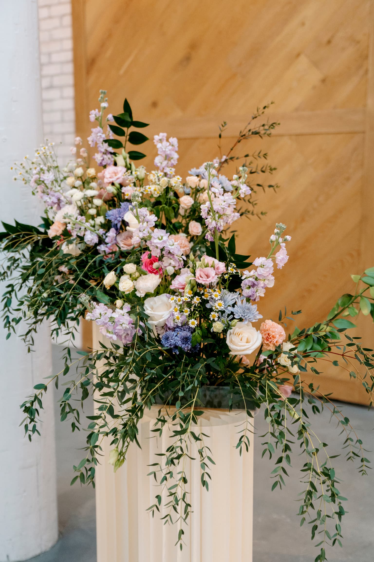 Pastel floral installation on a fluted pedestal against a wood backdrop