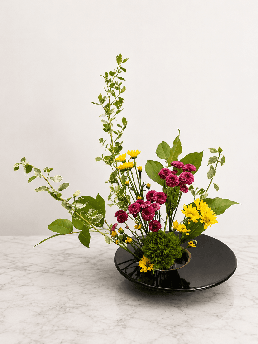 Ikebana arrangement of yellow daisies and magenta chrysanthemums in a black dish